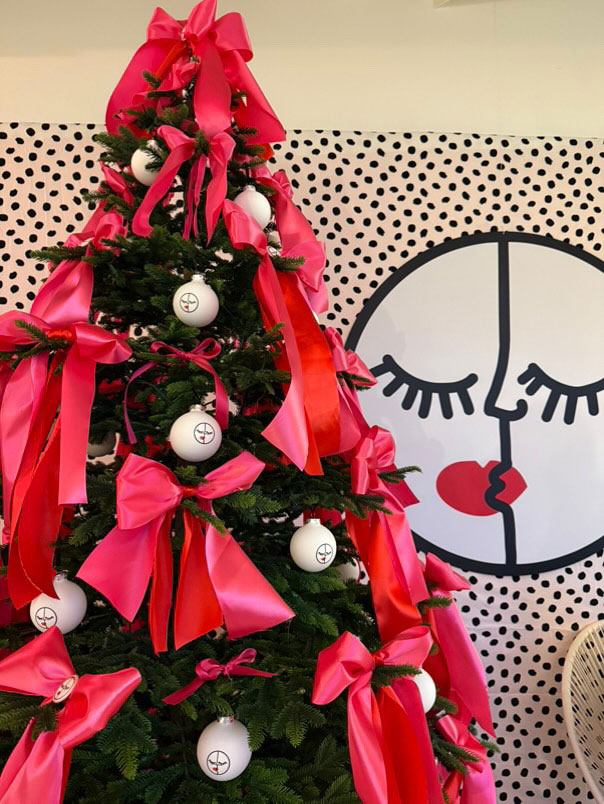 Pink-ribbon Christmas tree beside a smiling-face backdrop