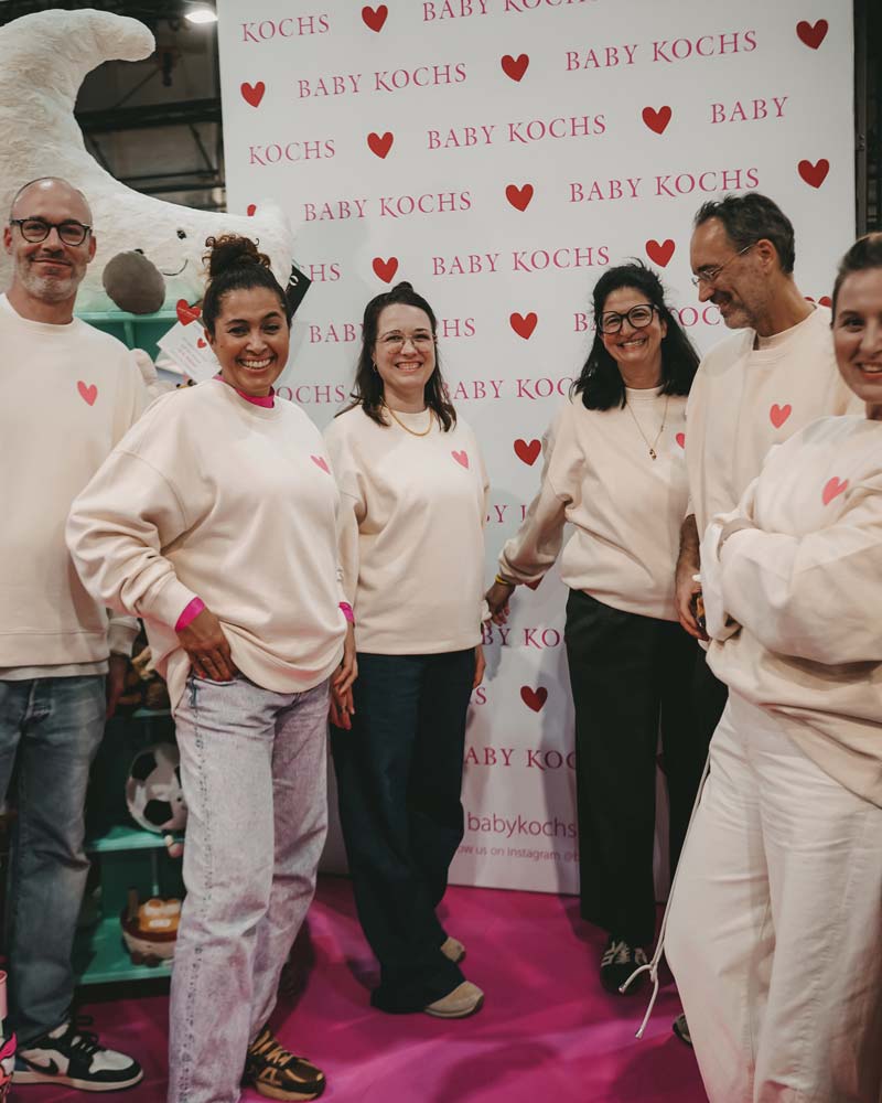 Exhibitor team in matching heart sweatshirts at the Baby Kochs wall