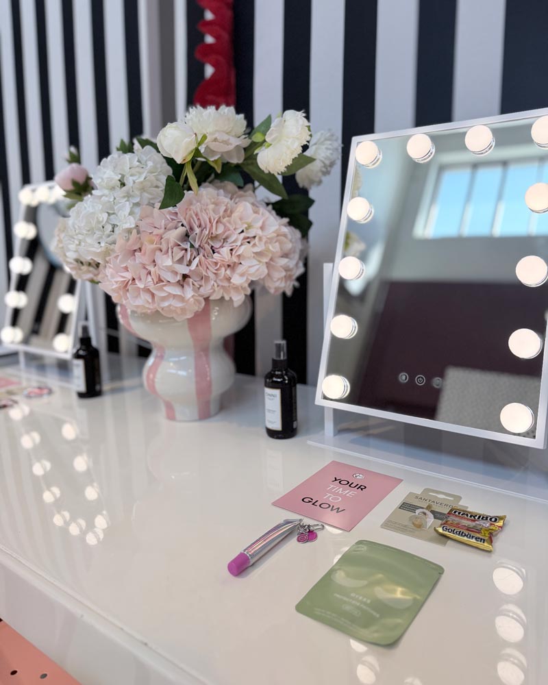Row of lit vanity mirrors with fresh flowers on a black-and-white dotted backdrop